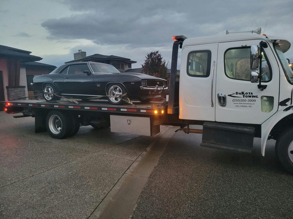 A black classic car loaded onto a tow truck.